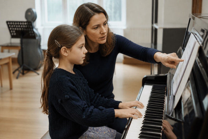 Klavierunterricht an einer Musikschule: Lehrerin zeigt einem Mädchen die Noten